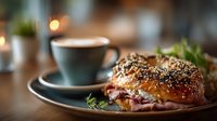 Gourmet sandwich with sesame seed bun and fresh herbs served alongside coffee cup on wooden table in cozy cafe setting for food photography and menu design.