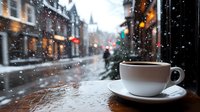 Hot coffee cup on wooden windowsill overlooking snowy winter street with bokeh lights and falling snowflakes. Cozy atmospheric evening cityscape through cafe window.
