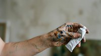 Tattooed hand holding white tissue or cloth, showing arm with colorful ink designs and patterns against blurred background for healthcare or hygiene concepts.