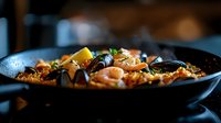 Traditional Spanish seafood paella with shrimp, mussels, and saffron rice in black cast iron pan, garnished with fresh herbs and lemon wedges, close-up view.