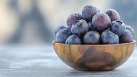 Fresh ripe blueberries covered with morning frost in wooden bowl on light background, macro food photography for healthy eating concept.