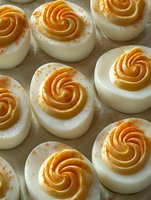 Deviled eggs topped with apricot jam swirls and cinnamon powder, arranged on parchment paper for entertaining or catering events.