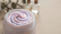 Swirled pink and white cosmetic cream or moisturizer in glass jar with blurred botanical background, suitable for beauty and skincare product marketing.