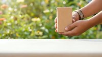 Person with medium skin tone holding kraft paper box outdoors with blurred green foliage background, suitable for e-commerce, shipping, delivery, and sustainable packaging concepts.