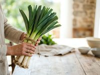 Fresh leeks held in hand with soil, ready for cooking or meal preparation in a bright kitchen setting.