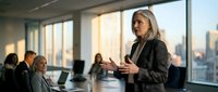 Senior Caucasian businesswoman leading a corporate meeting in a modern conference room with city skyline view, colleagues listening attentively.