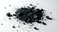 Pile of finely ground activated charcoal powder scattered on white surface, showing texture and particles for cosmetic, medical, or industrial applications.