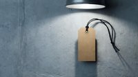 Blank kraft paper price tag with black string on textured gray surface under spotlight for retail branding and product labeling applications.