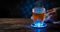 Steaming hot tea in transparent glass mug on wooden table with blue atmospheric lighting and cozy knit sweater sleeve visible in moody dark setting.