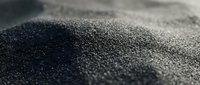 Close-up macro shot of fine black sand grains with shallow depth of field creating artistic blur effect for natural texture backgrounds and design projects.