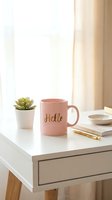 Pink ceramic mug with gold Hello lettering on a white desk with succulent plant, notebook, and gold pen in a bright cozy workspace.