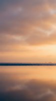 Serene coastal seascape at sunrise with calm waters reflecting golden and pink hues across the sky, distant fishing boats on horizon, peaceful dawn atmosphere for travel and nature projects.