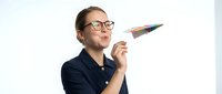 Young man with glasses and dark hair, wearing navy polo shirt, holding paintbrush against white background. Creative professional for art, design, and education projects.