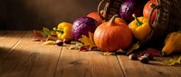 Autumn harvest cornucopia with pumpkins, colorful vegetables and fallen leaves spilling onto rustic wooden table in warm golden light for seasonal decor.