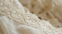 Delicate cream lace trim detail on soft fabric, showcasing intricate embroidered patterns and texture for wedding, fashion, and textile design projects.