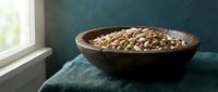 Wooden bowl filled with raw green lentils on teal fabric near window with natural light for healthy cooking and nutrition concepts.