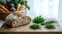 Fresh artisan sourdough bread with microgreens and organic vegetables on rustic wooden cutting board. Healthy farm-to-table cooking ingredients setup.