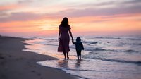 Mother and child walking hand in hand on beach at sunset with colorful sky and ocean waves creating peaceful family bonding moment for vacation memories.