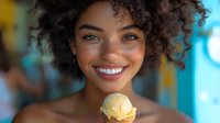 Young African American woman with natural curly hair and bright smile holding vanilla ice cream cone against vibrant turquoise background. Joyful summer lifestyle portrait.