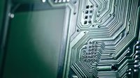 Green circuit board with intricate electronic pathways and microchip components for technology and computing applications.