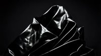 Black leather jacket with dramatic lighting and shadows creating artistic fashion photography composition for luxury apparel marketing materials.