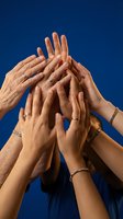 Multiple hands of diverse group reaching together in teamwork gesture against bright blue sky background symbolizing unity and collaboration.