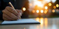 Female hand writing in notebook at sunset with golden bokeh lights in background, creating atmospheric mood for journaling, planning or creative writing.