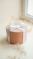 Round coral gift box with white ribbon bow on neutral background with soft lighting and decorative pearls for special occasions and celebrations.