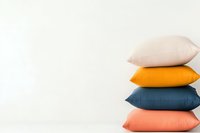 Minimalist stack of colorful decorative pillows in white, orange, navy blue and coral pink against plain white wall background with copy space.