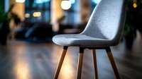 Modern gray upholstered dining chair with wooden legs against blurred restaurant interior background. Soft evening lighting creates cozy atmosphere. Suitable for furniture design.