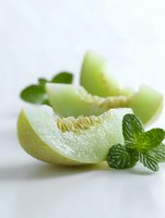 Fresh honeydew melon slices with mint leaves on white background, showcasing juicy texture and vibrant green color for food photography.