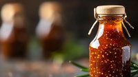Homemade chili oil in glass bottle with dried pepper flakes, sealed with cork and twine, blurred bottles in background.