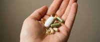 Caucasian hand holding white and green capsule supplements and pills for health, wellness, nutrition, and dietary supplement use.