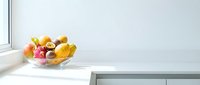 Fresh mixed fruits including apples, bananas, and oranges arranged in a glass bowl on a modern kitchen counter near a bright window.