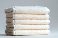 Stack of clean white folded cotton towels on light background, fresh hotel spa laundry with soft texture and neat layers for wellness and hygiene concept.