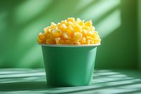 Fresh yellow corn kernels in green paper cup on green background with natural shadow pattern, minimalist food photography composition.