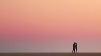 Romantic couple silhouette embracing against dreamy pink sunset sky gradient background for wedding invitations and love themed designs.