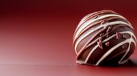 Gourmet chocolate truffle with white chocolate drizzle on deep red background, perfect for dessert advertising or confectionery marketing.