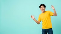 Cheerful young man with dark hair and East Asian ethnicity wearing bright yellow t-shirt dancing against turquoise background, expressing joy and positive energy for lifestyle and happiness concepts.