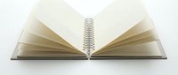 Open spiral-bound notebook with blank pages fanned out symmetrically, displaying metal coil binding and aged paper texture for education, writing, and study concepts.