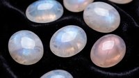 Polished moonstone gemstones with blue flash adularescence effect on dark surface for jewelry making and crystal healing practices.