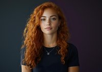 Young woman with natural red curly hair and freckles wearing black t-shirt against dark background, looking confidently at camera with subtle smile.
