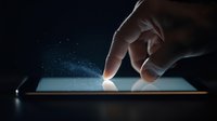 Hand touching glowing tablet screen with magical sparkles and light particles in dark environment, modern technology concept for digital interaction.