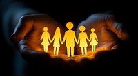 Glowing paper family silhouette held in caring hands against dark background, representing protection, unity and family support. Conceptual social welfare scene.