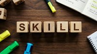 Wooden blocks spelling skill on dark wood desk with colorful markers, notebook and highlighters, representing professional development and training for business education.