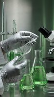 Scientist hands in gloves holding DNA double helix model in green-lit laboratory with microscope and chemical flasks for genetic research and biotechnology.
