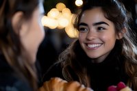 Young Hispanic woman smiling warmly during evening conversation with friend, cozy bokeh lights creating intimate atmosphere for social gatherings and connections.