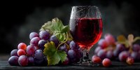 Red wine glass with fresh grapes and vine leaves on dark wooden table. Elegant alcohol beverage photography for restaurant menus and wine tasting events.