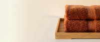 Rolled terracotta towels stacked in wooden tray on neutral background, spa and bathroom decor for hospitality, wellness and home interior design projects.