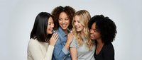 Diverse group of four happy women friends embracing and laughing together in casual clothing against white background for friendship and unity concepts.